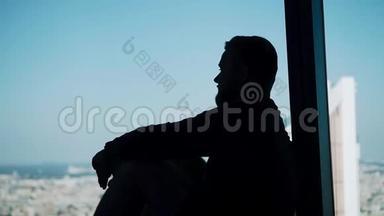 一个人坐在一个大的灯光窗户上的酷的轮廓。 凉爽厚重的气氛。
